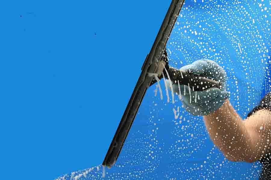 Expert window cleaning service provided by SoCal Cleaning Services. A professional window cleaner is seen from above, using a squeegee to clean a window on a high-rise building. 